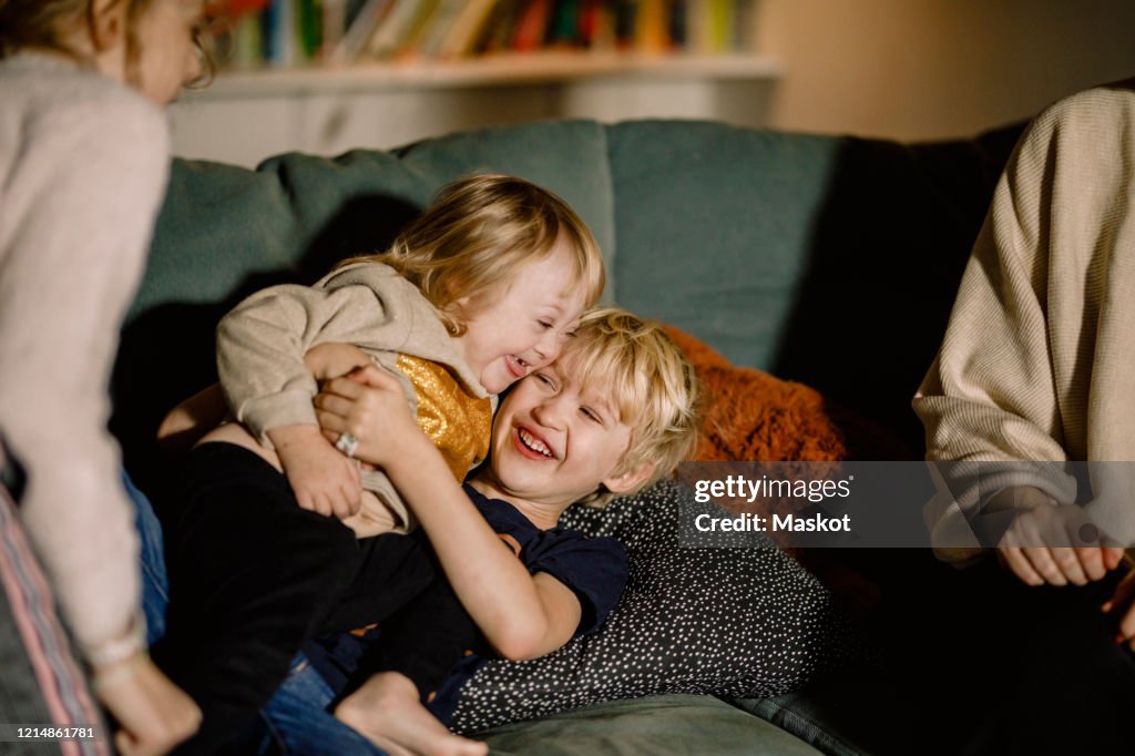 Brother holding sister with down syndrome while playing on sofa at home