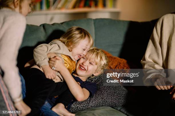 brother holding sister with down syndrome while playing on sofa at home - disabilitycollection fotografías e imágenes de stock