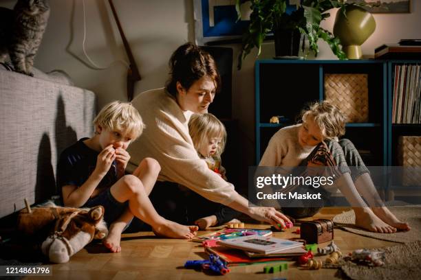 mother playing with children while sitting on floor at home - 4 people playing games stock pictures, royalty-free photos & images