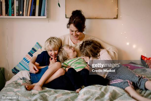 smiling disabled girl looking at mother while sitting by siblings in bedroom - disabilitycollection stock pictures, royalty-free photos & images