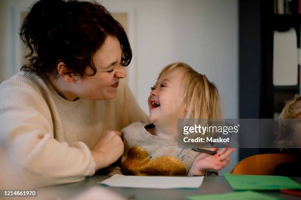 mother making facial expressions while playing with disabled daughter at dining table - down's syndrome stockfoto's en -beelden