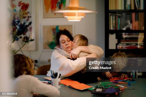 mother embracing girl with down syndrome while sitting by dining table at home - family drawing stock-fotos und bilder