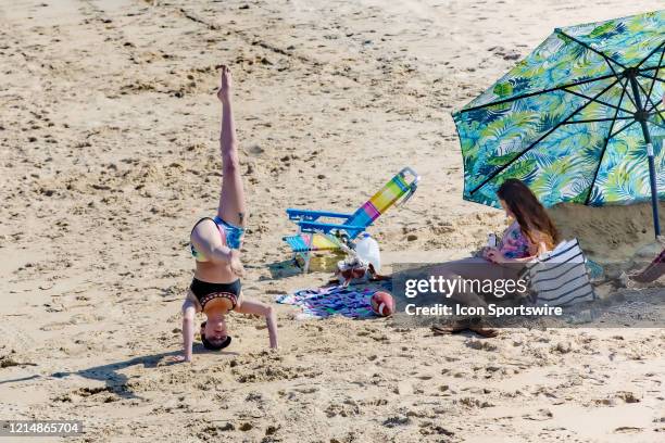 Woman stands on her head on the beach while a friend records her on Memorial Day weekend on May 22 in Virginia Beach, VA. This is the first day of...