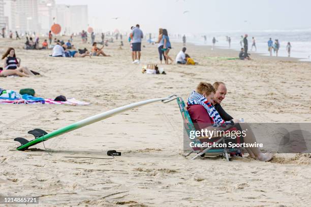 Two men with a surfboard propped up on the back of a chair relax and enjoy the beach on May 22 in Virginia Beach, VA. This is the first day of the...