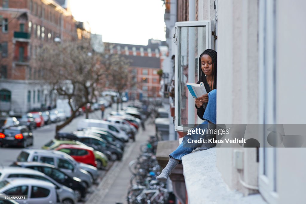 Young woman reading book in apartment window