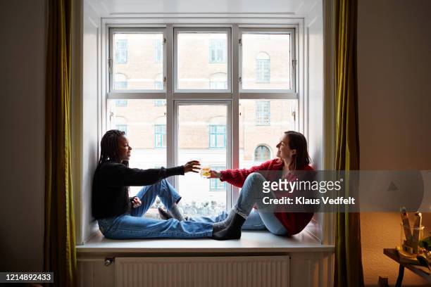young female roommates toasting cocktails in apartment window - northern europe stock pictures, royalty-free photos & images