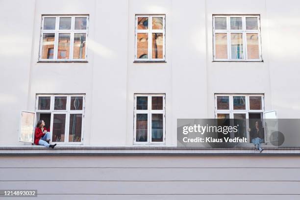 young female neighbors talking from apartment windows - social distancing friends stock pictures, royalty-free photos & images