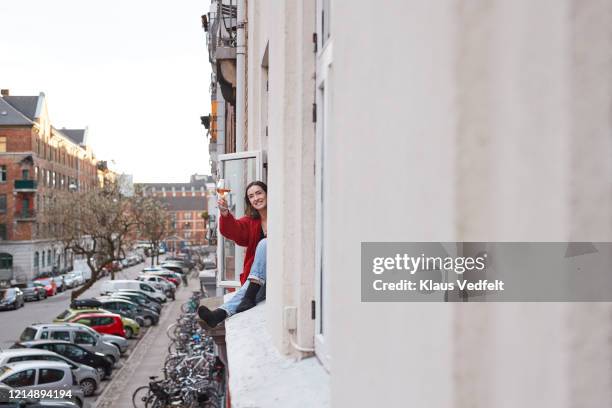 portrait happy young woman with wine in apartment window - lockdown window stock pictures, royalty-free photos & images