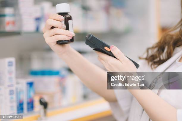 an asian chinese female pharmacist scanning on a bottle of pills for the pricing details at the cashier counter - labeling stock pictures, royalty-free photos & images