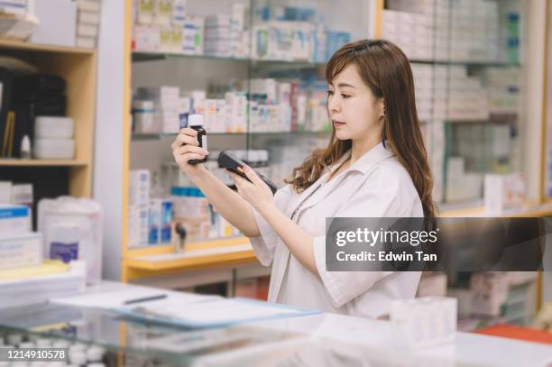 an asian chinese female pharmacist scanning on a bottle of pills for the pricing details at the cashier counter - sticking stock pictures, royalty-free photos & images