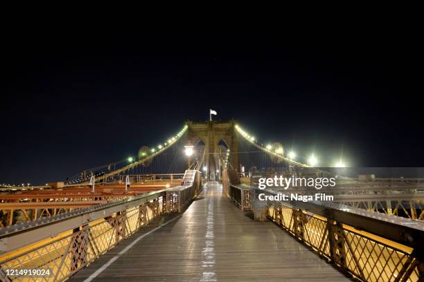 a wide angle shot on the brooklyn bridge at night with no people and no cars. lonely street scenes during the covid-19 / corona virus shutdown in new york city at night. - brooklyn bridge photos et images de collection