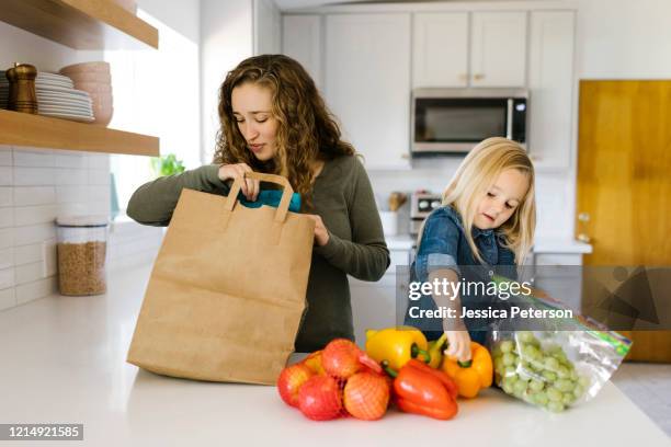 mother and daughter unpacking groceries - young man groceries kitchen stock-fotos und bilder