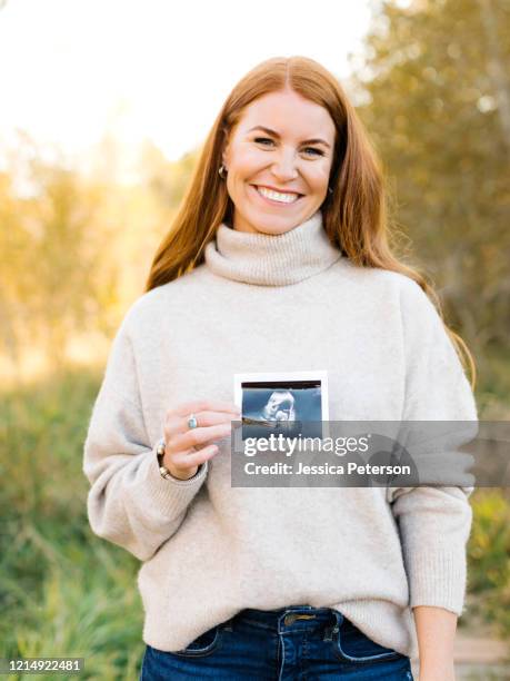 smiling pregnant woman holding ultrasound photograph - pregnant redhead ストックフォトと画像