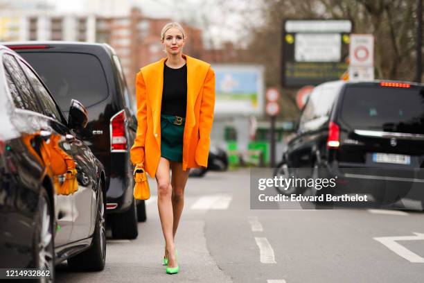 Leonie Hanne wears an orange oversized blazer jacket with large lapels, a black top, a green mini Balmain skirt with a belt, a yellow Balmain bag,...