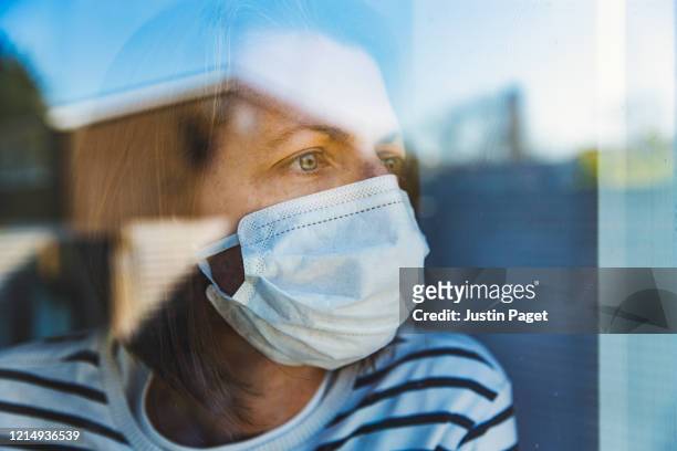 woman in mask looking through window - pandemic illness stockfoto's en -beelden