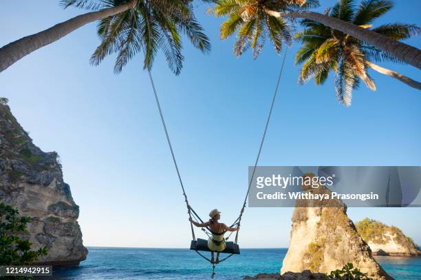 young caucasian woman on the swing with view of diamond beach in nusa penida bali - bali stockfoto's en -beelden