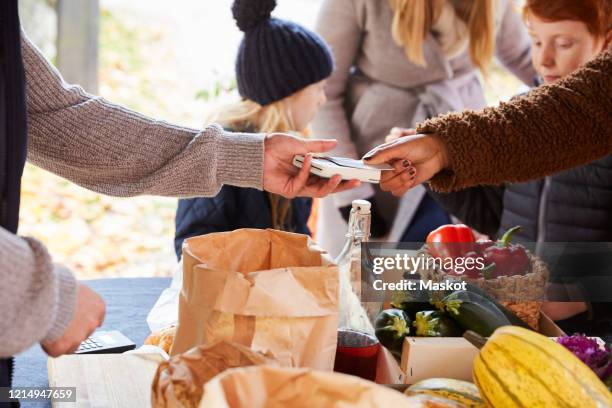 woman paying through credit card to male vendor at market stall - paying supermarket stock pictures, royalty-free photos & images