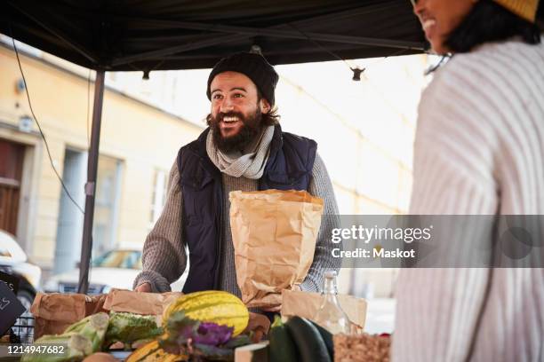 smiling man buying vegetables from female vendor at market stall - markets stock-fotos und bilder