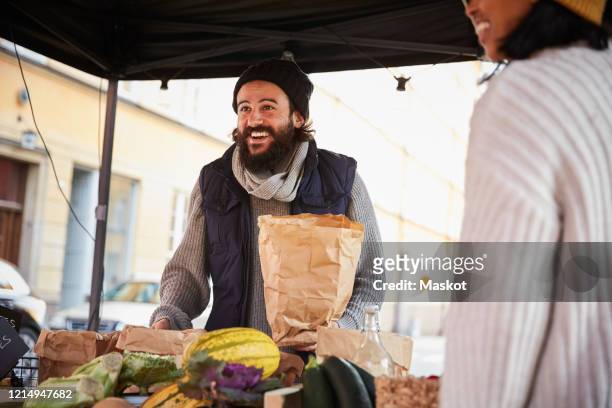 smiling man buying vegetables from female vendor at market stall - autumn sale stock pictures, royalty-free photos & images