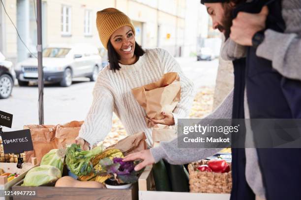smiling woman buying fresh vegetables from male market vendor at fruit stall - winter vegetables stockfoto's en -beelden
