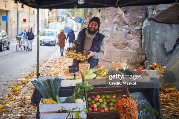 portrait of happy man standing with vegetable basket at market stall - marché de plein air photos et images de collection