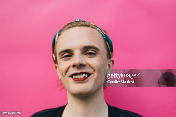 portrait of smiling confident young man standing against pink background - non binary stereotypes stock pictures, royalty-free photos & images