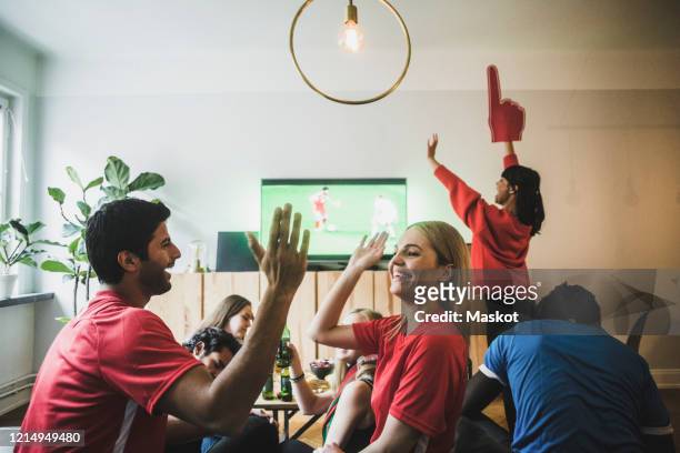 smiling man and woman high-fiving while celebrating victory with friends at home - match sportivo foto e immagini stock