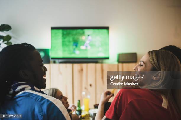 smiling male and female watching soccer while sitting with friends at home - back in the game stock pictures, royalty-free photos & images