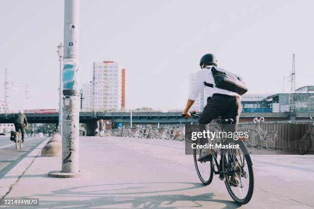 rear view of businessman riding bicycle on sidewalk against clear sky in city - räder stock-fotos und bilder
