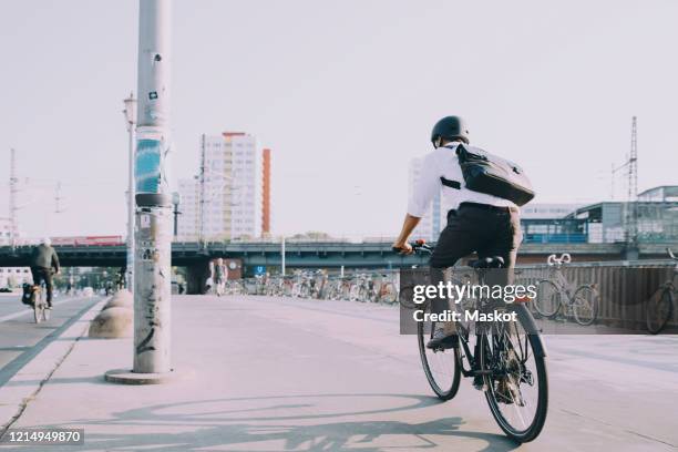 rear view of businessman riding bicycle on sidewalk against clear sky in city - bicycle stock-fotos und bilder