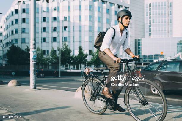 full length of businessman riding bicycle on sidewalk against building in city - verkehrsweg für fußgänger stock-fotos und bilder