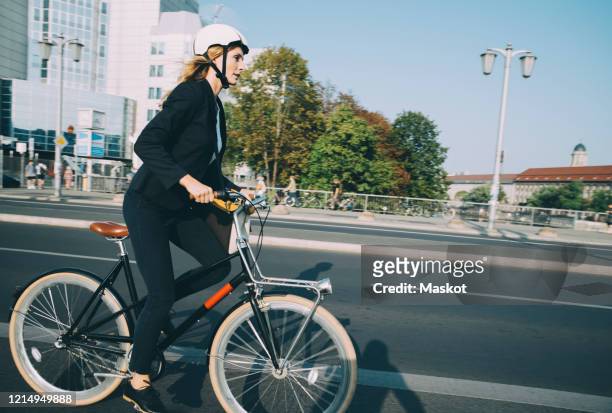 side view of businesswoman riding bicycle on city street against sky - cycling helmet stock-fotos und bilder