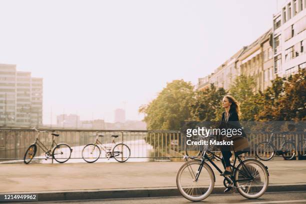 full length of female professional riding bicycle on road in city against sky - radfahren stock-fotos und bilder
