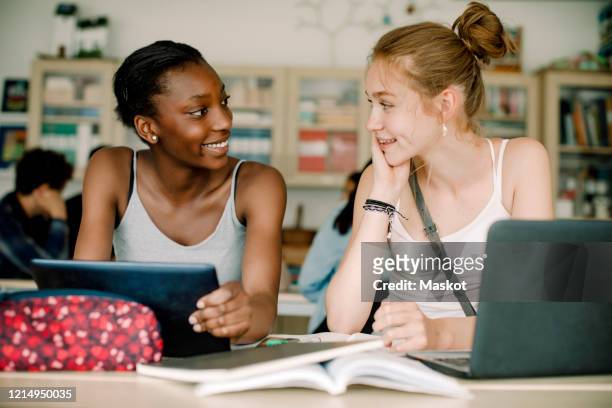 smiling teenagers talking while sitting by table in classroom - sweden school stock pictures, royalty-free photos & images