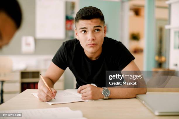 contemplating teenage boy looking away while sitting in classroom - boy thinking stock-fotos und bilder