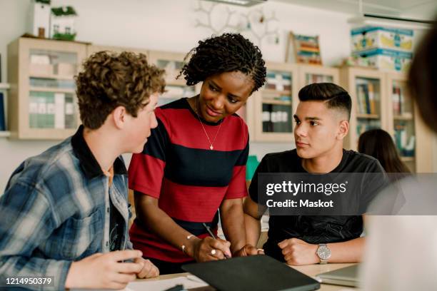 female professor discussing with male students while standing in classroom - male professor with students fotografías e imágenes de stock