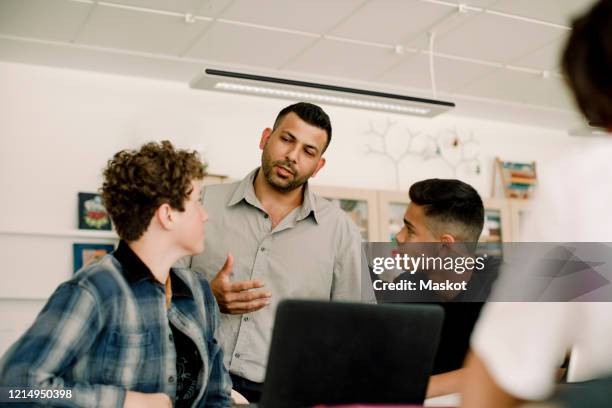 professor discussing with male students while standing in classroom - male teacher in a classroom stock-fotos und bilder