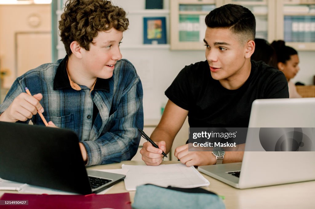 Male students talking while sitting by table in classroom