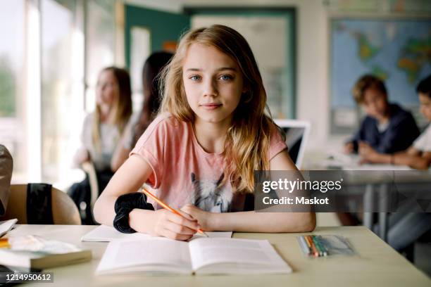 portrait of female student writing in book while sitting at table in classroom - child in classroom stock pictures, royalty-free photos & images