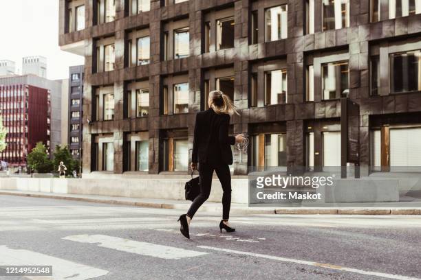 rear view of businesswoman crossing street against building - vestimenta de negocios formal fotografías e imágenes de stock
