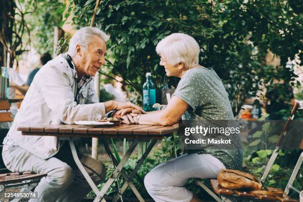 senior couple holding hands talking while sitting at restaurant in city - old couple restaurant stock-fotos und bilder