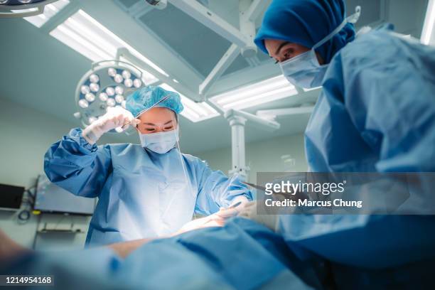 アジアの多民族女性外科医チームは、病院の手術室で患者の脚に外科的ステッチを操作します - medical stitches ストックフォトと画像