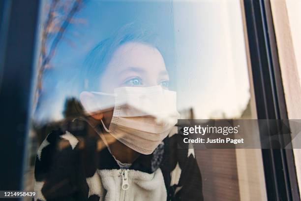 young girl with mask looking through window - pandemic illness stockfoto's en -beelden