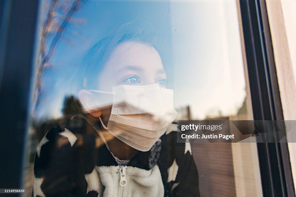 Young girl with mask looking through window