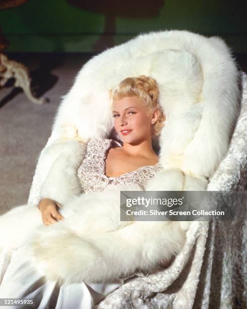 Rita Hayworth , US actress and dancer, with blonde hair, posing on a white fur-lined chair, in a publicity portrait issued for the film, 'The Lady...