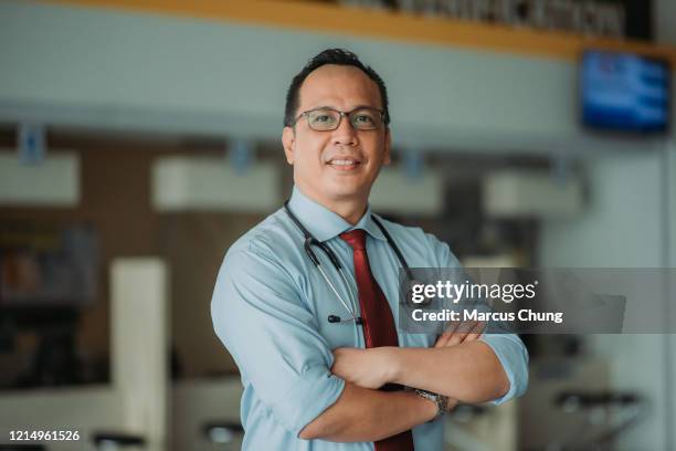 portrait of malay male doctor arms crossed with smiling face and looking at camera standing at entrance lobby of hospital - doctors arms crossed stock pictures, royalty-free photos & images