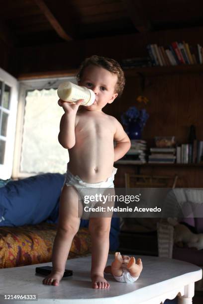 baby boy shirtless drinking bottle with brown curly hair and brown eyes chubby cheeks small hands pale complexion - funny baby photo - fotografias e filmes do acervo