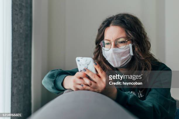 besorgte frau liest nachrichten am telefon - pandemic illness stock-fotos und bilder