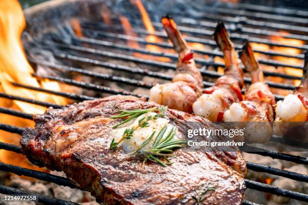 ein köstliches ribeye steak und speck gewickelt garnelen auf einem flammenden heißen grill - vom holzkohlengrill stock-fotos und bilder