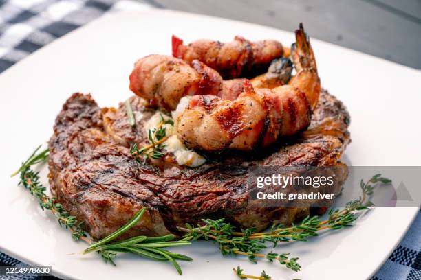 bistecca di ribeye alla brace con timo e rosmarino con gamberi jumbo avvolti in pancetta o gamberi su un piatto, pronti da mangiare - shrimp foto e immagini stock